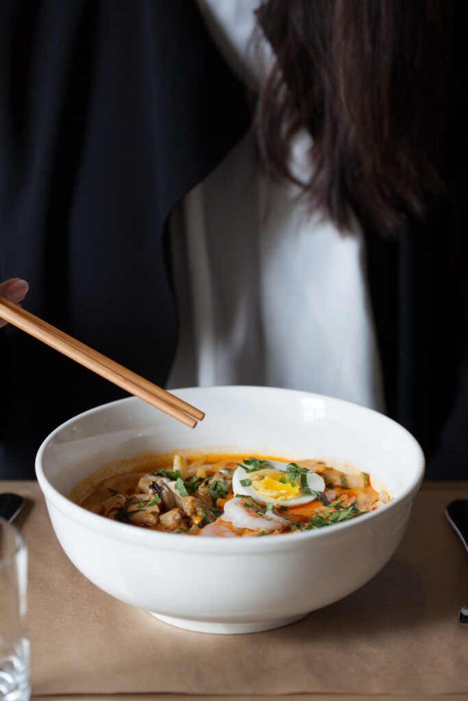 A bowl of Laksa and woman with chopsticks